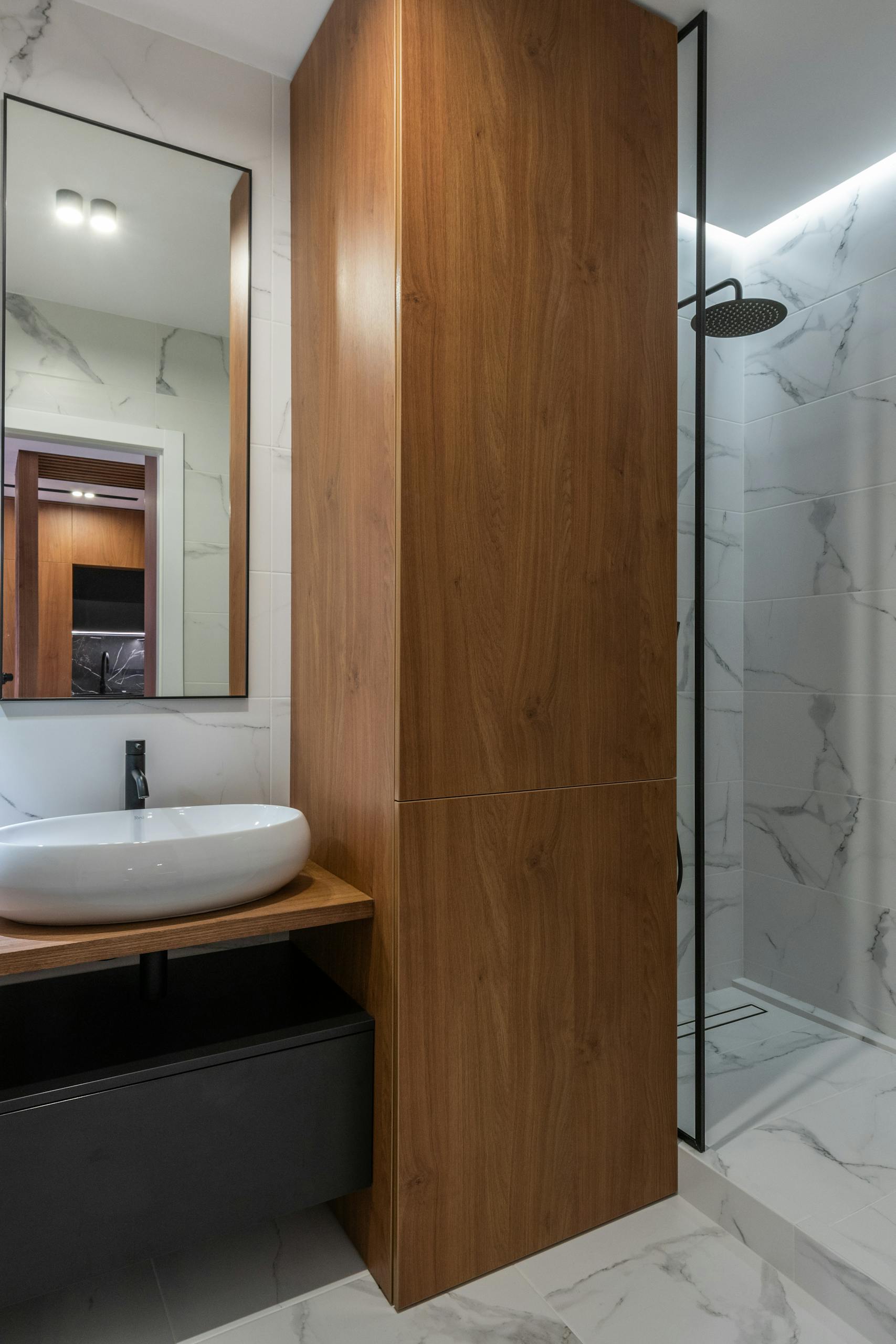 Sleek modern bathroom featuring a wooden cabinet, marble tiles, and a stylish shower area.